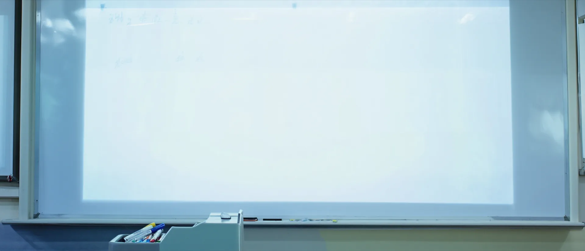A wide whiteboard in a bright tutoring room, with a tray of markers and a board eraser in the foreground